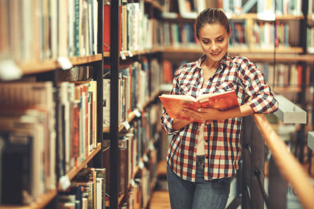 istock Young female student read and learns by the book shelf at the library. 1164704422
