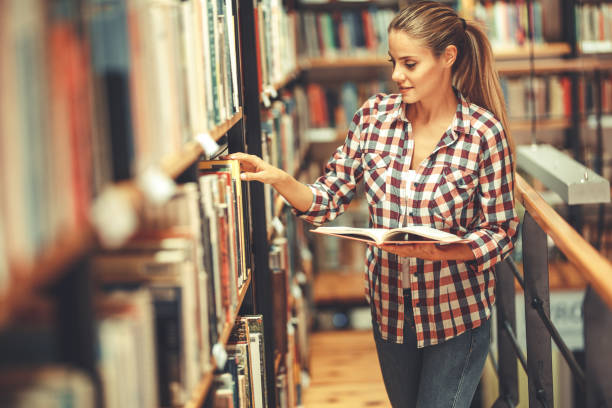 istock Young female student read and learns by the book shelf at the library. 1164704565