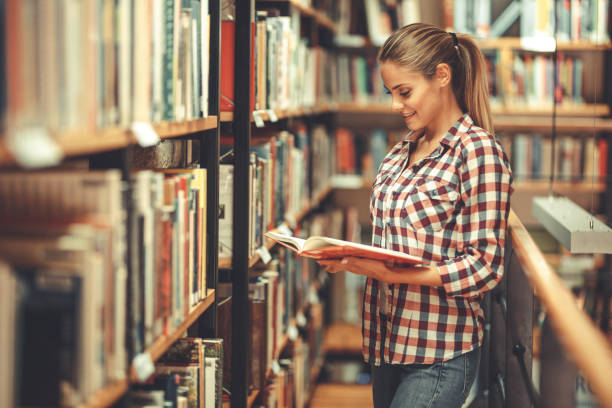 istock Young female student read and learns by the book shelf at the library. 1164704605