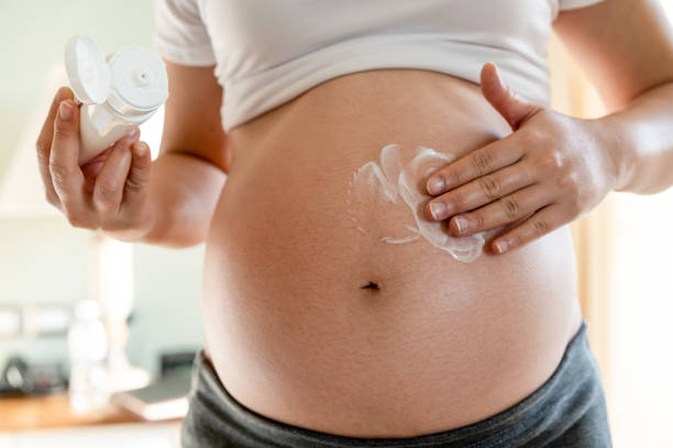 femme enceinte heureuse appliquer lotion crème de soins de la peau sur le ventre enceinte pour prévenir la marque d'étirement. traitement de massage de peau sain et concept de soin d'humidité. - human pregnancy abdomen human skin healthcare and medicine photos et images de collection