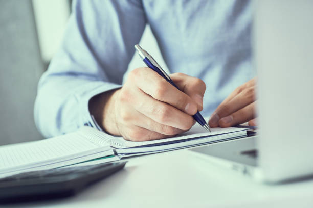 istock Businessman hand writing note on a notebook. Business man working at office desk. Male office worker writes information in a notebook. 1164707938