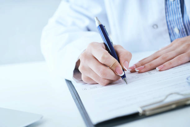 Female medicine doctor hand holding silver pen writing something on clipboard closeup. Medical care, insurance, prescription, paper work or career concept. Physician examining patient. la mano de la doctora de medicina femenina sosteniendo la pluma de plata escribiendo algo en el primer plano del portapapeles. mucho trabajo de papel en medicina. ronda de barrio, verificación de la visita del paciente, cálculo médico y concepto de esta