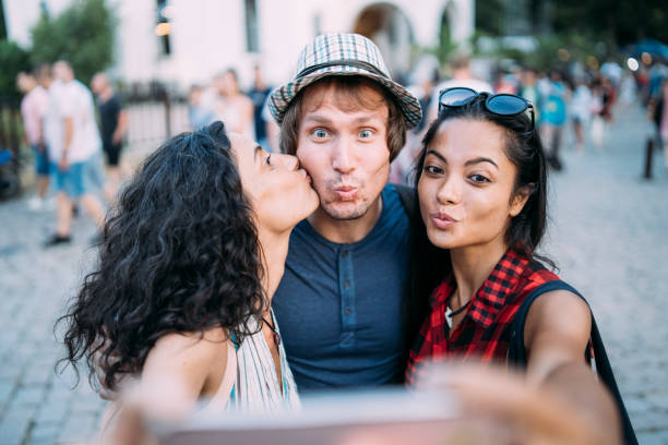 Friends taking selfie and giving a kiss Friends taking selfie on street and giving a kiss. three way kiss stock pictures, royalty-free photos & images