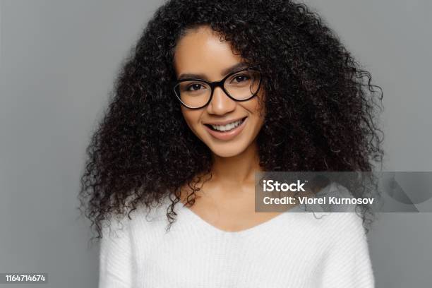 Headshot Of Curly Haired Smiling Woman Has Healthy Dark Skin Afro Hairstyle  Smiles Gently At Camera