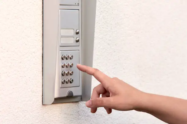 The hand of a young woman enters a numeric code on the keypad of an electronic lock or doorbell.