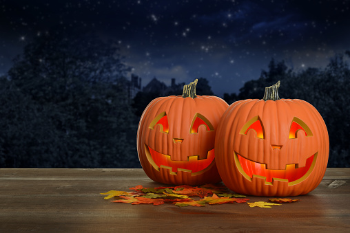 two Halloween pumpkins at night glowing on wood table with fall leaves