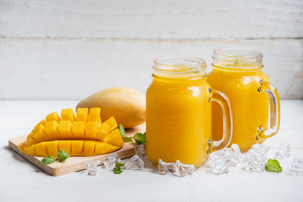 istock Refreshing mango smoothies in glass with ripe mango on white wooden table 1164728913