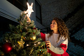 Happy woman decorating her Christmas tree and putting the star on top