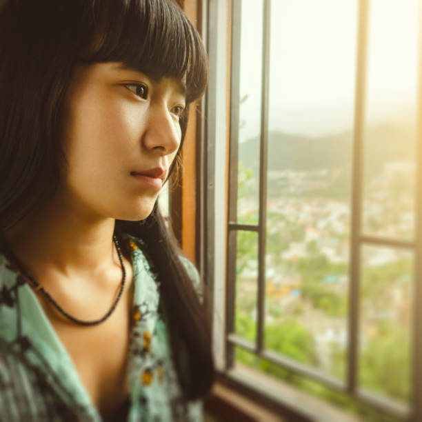 istock Young woman contemplates and looks at view through a window. 1164732063