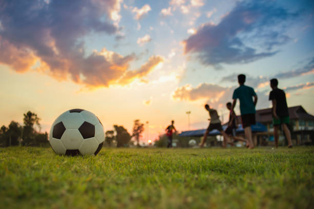 夕暮れの夕日の空の下でコミュニティ農村地域で運動のためにサッカーサッカーを楽しんでいる子供たちのグループの屋外シルエットアクションスポーツ。 - ball horizontal outdoors childhood ストックフォトと画像