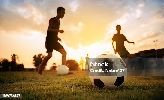 istock Silhouette action sport outdoors of a group of kids having fun playing soccer football for exercise in community rural area under the twilight sunset sky. 1164736873