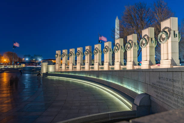 A photograph of the World War II Memorial at sunset. The Memorial is located on the National Mall in Washington, DC and is the first national memorial dedicated to all who served during World War II. It is located on 17th Street, between Constitution and Independence Avenues, and is flanked by the Washington Monument to the east and the Lincoln Memorial to the west. This photo was taken at sunset.