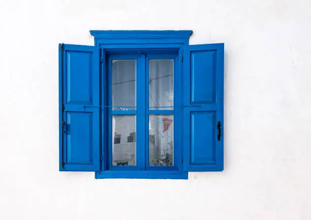 Photo of Blue window with open shutters and white wall of greek house in Amorgos, Greece.