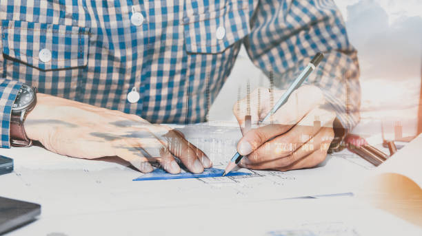 istock architects,engineer holding pen  equipment On the desk with a blueprint in the office.Double exposure,drawing and a new house structure plan background. 1164737003