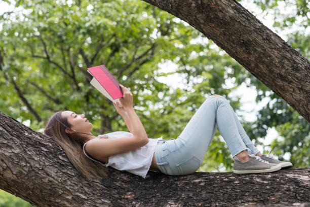 istock Attractive girl read book on tree trunk 1164747803