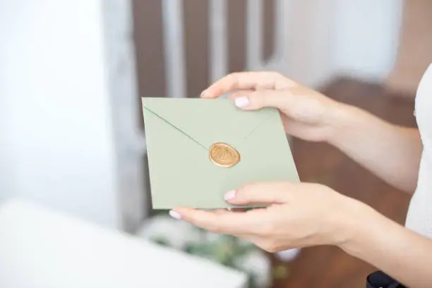 Photo of Close-up photo of female hands holding invitation envelope with a wax seal, a gift certificate, a postcard, wedding invitation card.