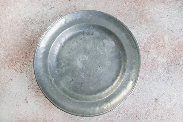 Vintage pewter plate on a concrete background. Copy space for text.