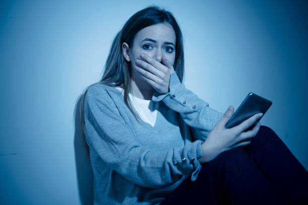 Sad desperate young teenager female girl on smart phone suffering from online bulling and harassment felling lonely and hopeless sitting on bed at night. Cyberbullying technology and dangers of internet concept. triste joven adolescente adolescente adolescente chica en el teléfono inteligente que sufre de toros en línea y acoso talando solitarias y desesperadas sentadas en la cama por la noche. tecnología de ciberacoso y peligros del concepto de internet.