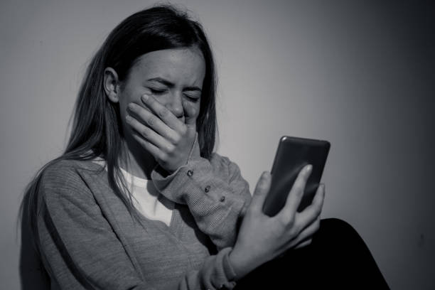 Sad desperate young teenager female girl on smart phone suffering from online bulling and harassment felling lonely and hopeless sitting on bed at night. Cyberbullying technology and dangers of internet concept. triste joven adolescente adolescente adolescente chica en el teléfono inteligente que sufre de toros en línea y acoso talando solitarias y desesperadas sentadas en la cama por la noche. tecnología de ciberacoso y peligros del concepto de internet.