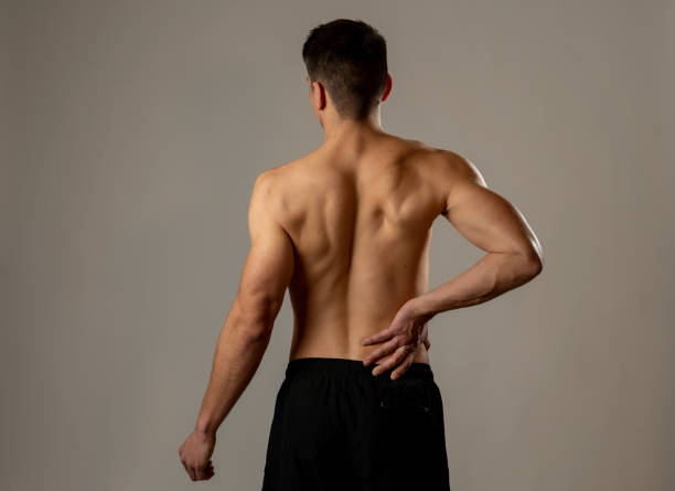 jeune homme de forme physique musculaire touchant et saisissant son bas du dos souffrant la douleur forte après séance d'entraînement. isolé sur le fond neutre. dans les blessures sportives problèmes de posture incorrecte et soins de santé du corps. - bas du dos photos et images de collection
