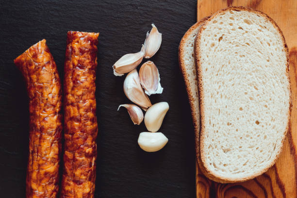 istock Two sausages next to garlic and a wooden cutting board with white bread slices 1164760607