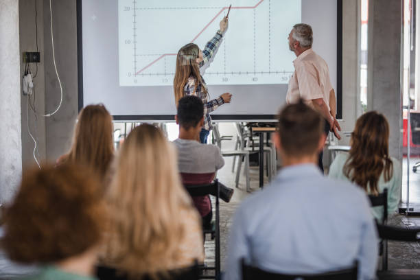 istock Female student giving a presentation in front of projection screen in lecture hall. 1164763523