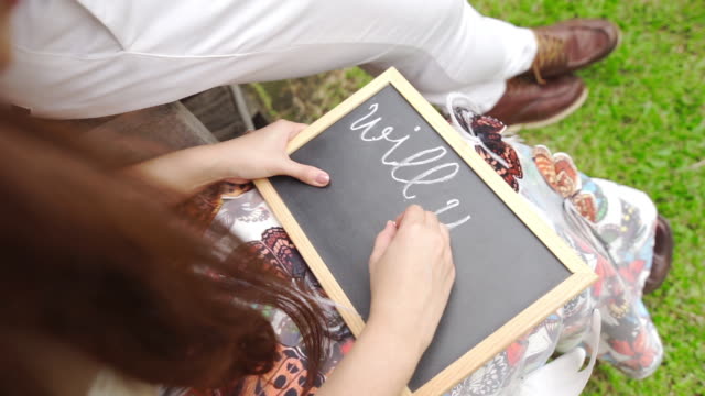 Handwriting on a blackboard with the text “Will you marry me question” written on it.