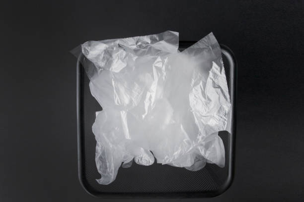 istock Plastic bag with handles, gloves in the bin on a black background . Used plastic bag for recycling. Concept - ecology, planet pollution with plastic cellophane polyethylene 1164779519