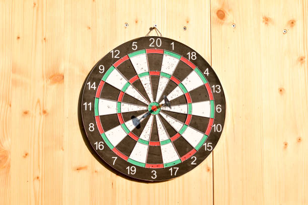 Close-up of an electronic dartboard illuminated in dim lighting. The dartboard's bullseye and surrounding scoring areas are visible, showcasing intricate patterns and numbers. Soft shadows create a moody atmosphere, highlighting the details of the game device.