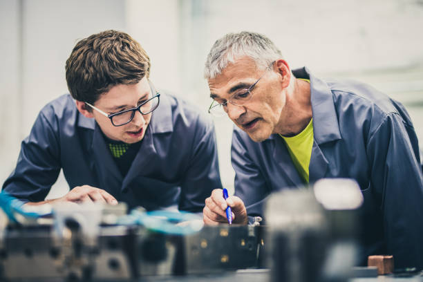 Senior engineer explaining machine functioning to his student Senior engineer mentoring his student by explaining the functioning of a machine and pointing to its parts. mentorship stock pictures, royalty-free photos & images