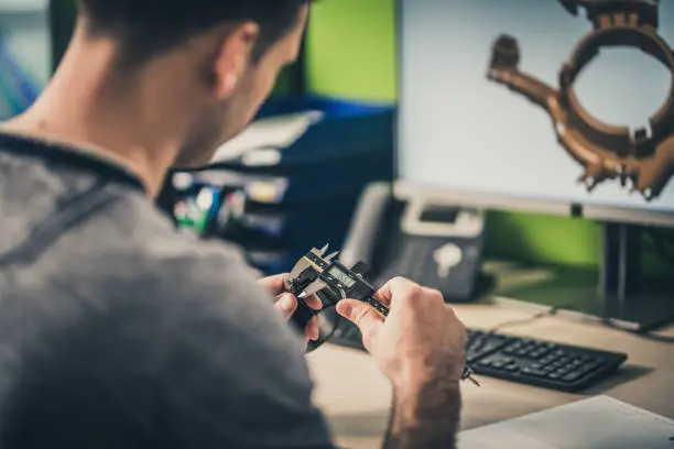 Photo of Engineer measuring a machine part while working on a 3D model