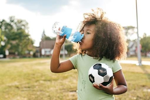 Smiling girl outside with bottle of water and soccer ball