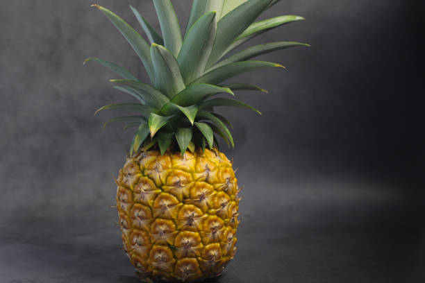 istock Single whole yellow pineapple with leaves on neutral tan background, whole pineapple tropical fresh fruit food photography 1164790972