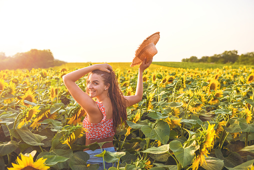 happy girl with a straw head on a head in a sunflower field with arms raised