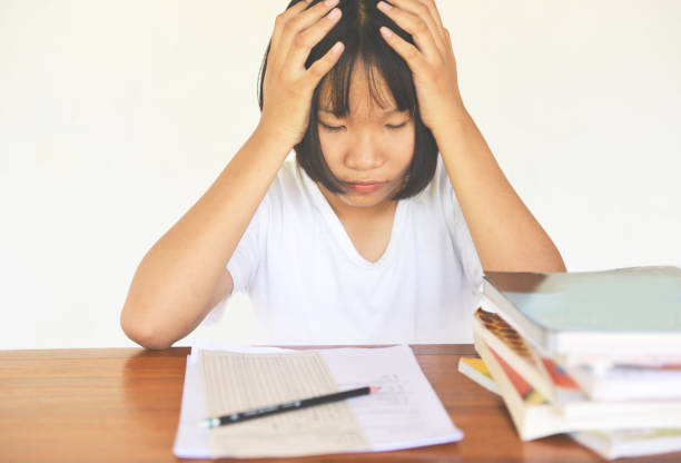 istock exam stress - education young female college in class taking notes and using a pencil sitting learning concept stressed student girl asian take the exam final with books on the table 1164796447