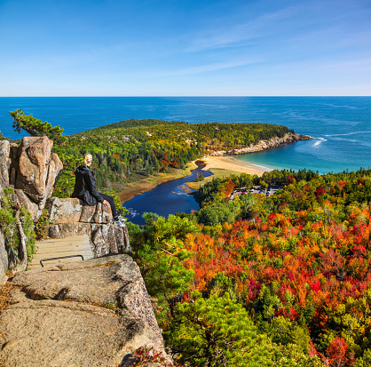 Female hiker sitting on ledge enjoying view of water from Beehive Trail in Acadia National Park