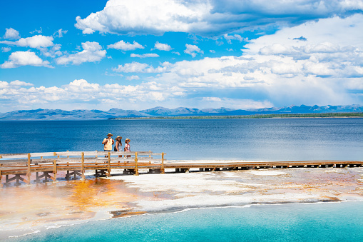 Family relaxing and enjoying beautiful view of hot spring on vacation hiking trip. Beautiful Yellowstone Lake in the background and hot spring in foreground. Yellowstone National Park. Wyoming, USA