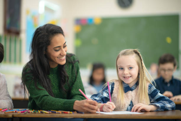 istock Teacher helps her female blonde student with her assignment in class 1164801532