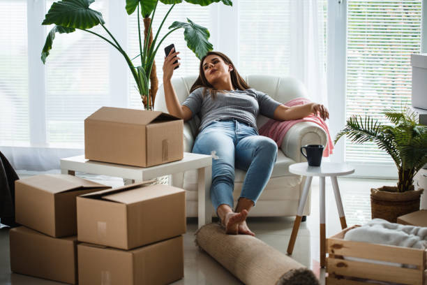 istock Woman using phone while resting on armchair in her new apartment 1164802100