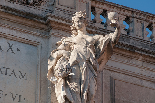Rome, Italy - September 20, 2013: Statue of woman representing the autumn harvest with grape vine and wine goblet in her hands. Top of Palazzo Poli of Trevi Fountain