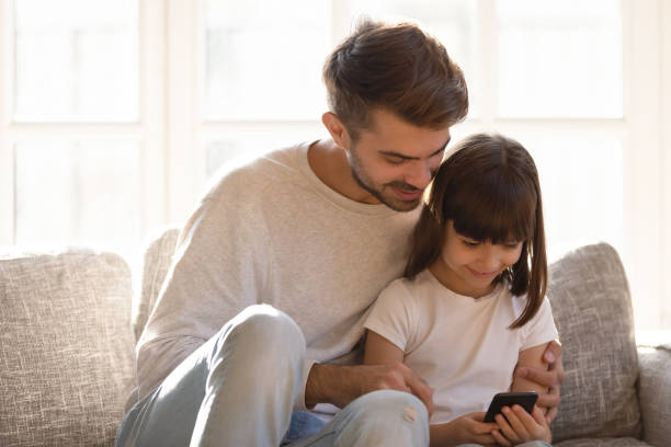 istock Young father relax using smartphone with little daughter 1164802807