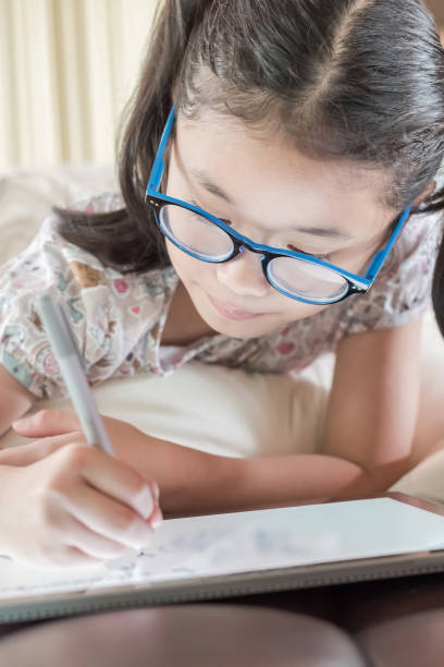 Asian school child girl with eyeglasses using tablet device drawing on touchscreen surface