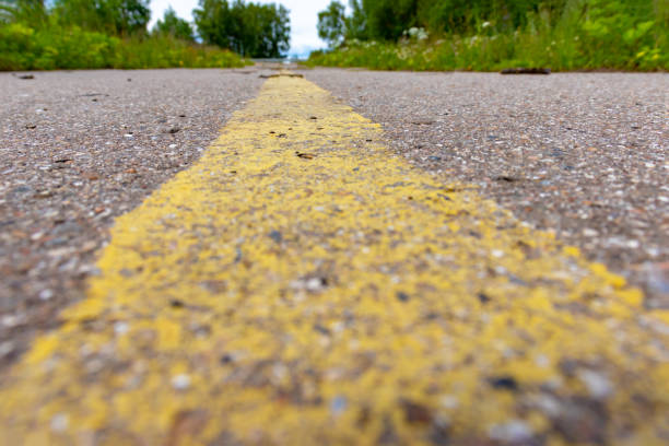 istock Yellow solid line, grunge road marking on asphalt close up with rural landscape on background 1164834095