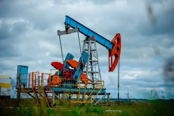 Oil field with pump jack, profiled on blue sky with white clouds, on a sunny day in spring