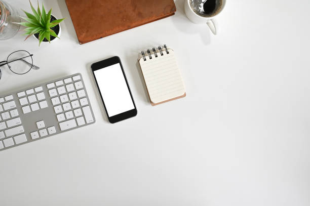 istock Top view office desk mockup smartphone, computer keyboard, coffee, notepad paper on white table. 1164836964