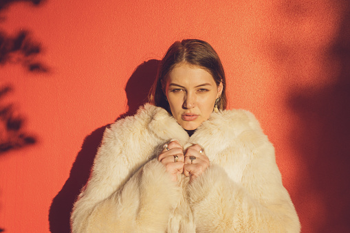 Young Woman Wearing Fake Fur Coat Against Orange Wall In Urban Location