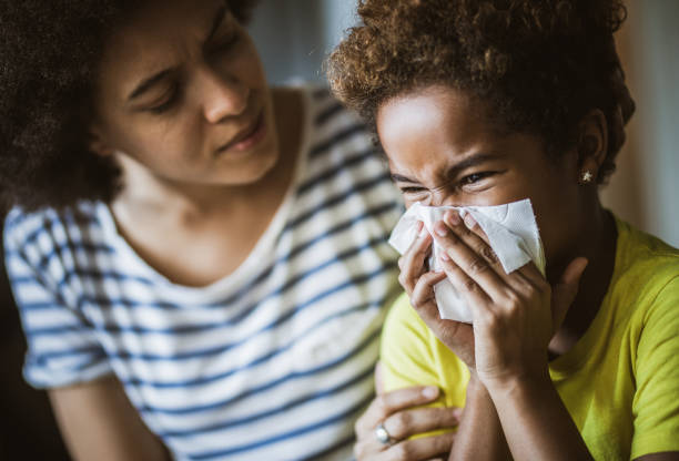 Black mother consoling her daughter who is blowing a nose. Ill African American girl blowing a nose at home while her mother is consoling her. blowing nose photos stock pictures, royalty-free photos & images