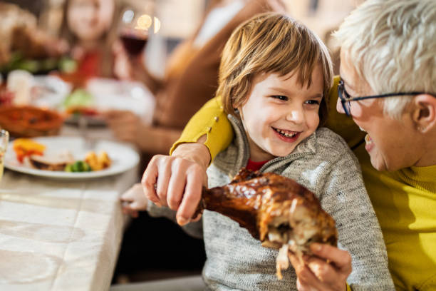 istock Happy boy talking to his grandmother while eating turkey leg at dining table. 1164844918