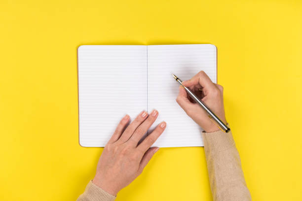 istock Woman's hands with perfect manicure holding pencil and  notepad as mockup for your design. Yellow background, flat lay 1164847686