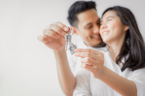 Happy Asian couple embracing and showing key to new home